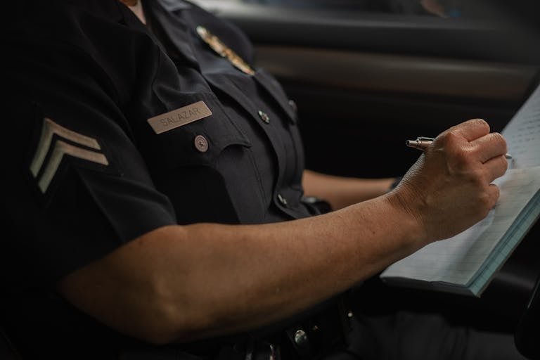 Close-up of a police officer writing in a notebook while sitting in a car, focused detail.